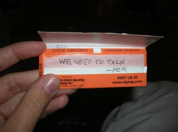A teenager holds a box of zig zags where his mom has written "we need to talk."