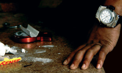 A hand on a counter next to a grinder, rolling papers, and a white powder. A scene from the movie How To Make Money Selling Drugs