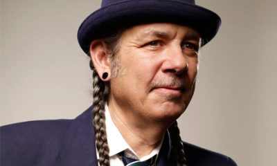 A portrait of "Weed War's" host Steve Deangelo wearing a bowler hat, two long braids, gauges and a blue suit.