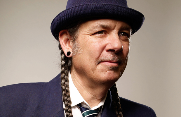 A portrait of "Weed War's" host Steve Deangelo wearing a bowler hat, two long braids, gauges and a blue suit.