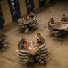 Prisoners in striped apparel sitting at tables playing cards.