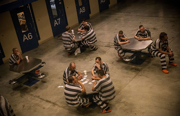 Prisoners in striped apparel sitting at tables playing cards.