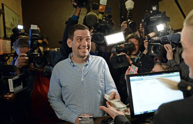 An excited customer hands over his money as cameras watch on while he makes the first retail marijuana purchase in American history.