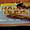 The cover of the book Happy Buds atop a bamboo placemat. On top of the book is a Zippo and an unrolled blunt.