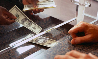 A banker hands a customer 100 dollar bills through a teller window.