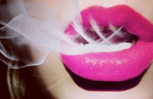 A woman with bright pink lips exhales a hit from marijuana, which allows her to have a better sex life.