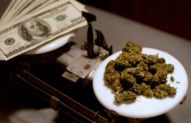 A scale holds stacks of 100 dollar bills on one side and buds on the other are even in states where MMJ is legal. MMJ states are set to rake in massive revenue from the cannabis industry.