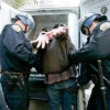 Man in handcuffs being placed into the back of a van by two police officers