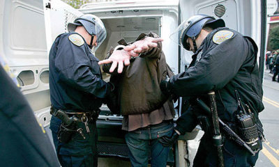 Man in handcuffs being placed into the back of a van by two police officers