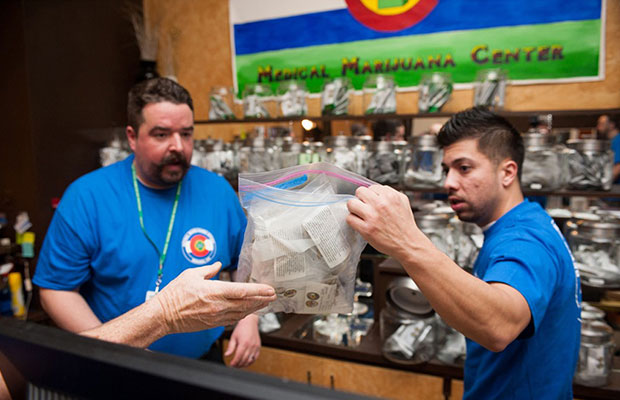 Two budtenders in Colorado give a customer a ziploc bag full of legal, recreational marijuana product, cashing in on more than $2 million dollars of recreational sales in the first month.