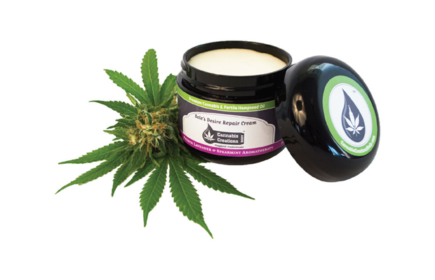 A pot of body butter by Cannabis Creations sits on top of and next to a pot leaf and flower.