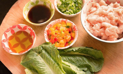 Lettuce, oil, peppers, soy sauce and chicken sit it bowls on table.
