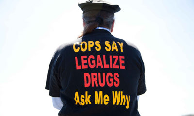 A man in a cop hat and shirt that says "Cops Say Legalize Drugs Ask Me Why."