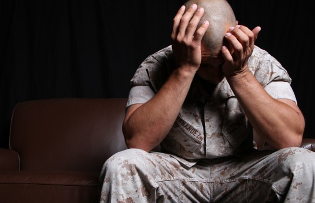 A veteran in camp holds his heads in his hands as he suffers an episode of PTSD, which now can be treated by MMJ in Michigan.
