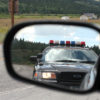 A police car in the rear view mirror of a vehicle that has been racially profiled and pulled over on the false accusation of holding marijuana.