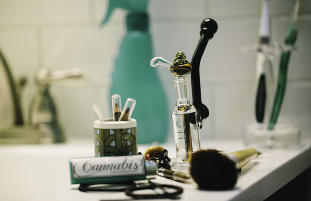 A Purr Mini-Bong sits on a bathroom counter along with a lighter and makeup items.