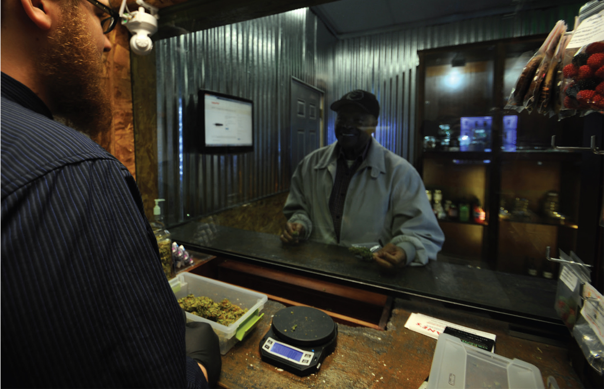 A patient in a gray coat asks a bud tender at the Seattle Greenlight Care Center in Washington for his medication.