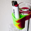 A multi-colored silicone Lighter Buddy by Elevated Concepts. is conveniently strapped to a bong and holds a lighter for easy smoking.