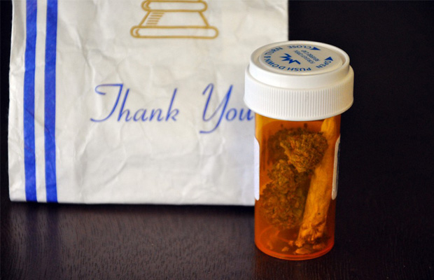 Prescription bottle in front of a "Thank You" prescription bag. In the bottle is a couple of nugs and a joint from a dispensary in Massachusetts