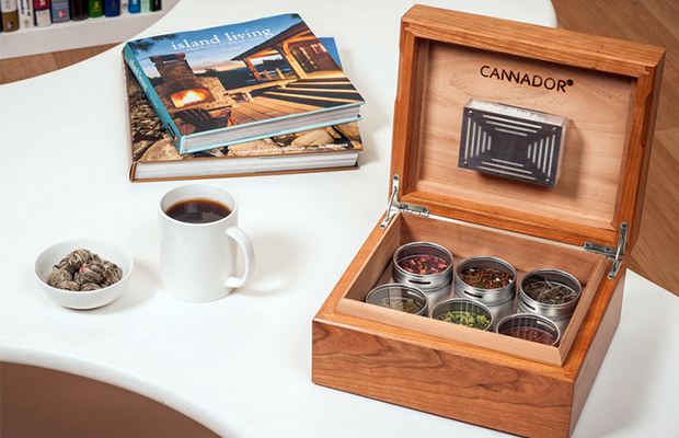 A Cannador box, a take on cigar humidors for cannabis, sites on a white table next to a cup of coffee and magazines.