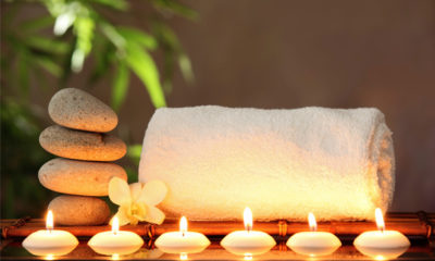 Tea candles float in water in front of fluffy white towel next to soothing hot stones. All topped off with a small yellow daffodil at a cannabis spa.