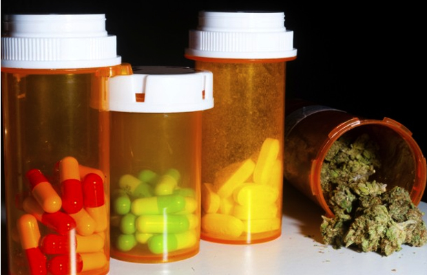 Three pill bottles are filled with opioids often prescribed for pain management despite many overdoses/year. A 4th bottle contains a safer option, marijuana.