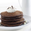 A stack of double chocolate infused pancackes are topped with a dollop of whipped cream.