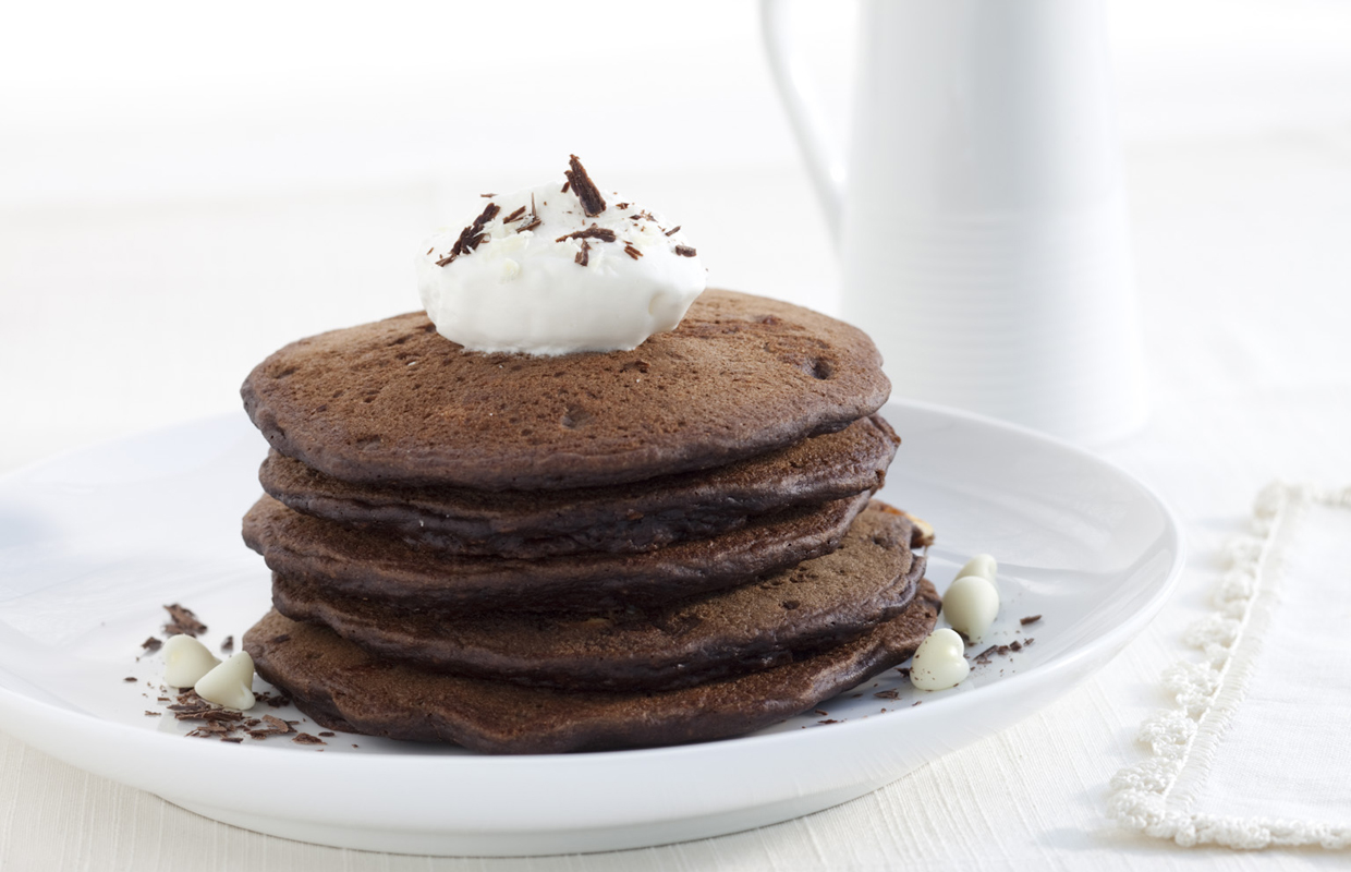 A stack of double chocolate infused pancackes are topped with a dollop of whipped cream.