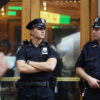 Two NYPD officers stand outside a door as they look to complete arressts other than "buy and bust" arressts.
