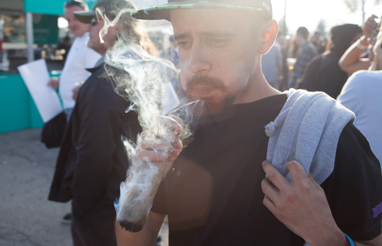 A man at a Cannabis Cup takes a hit from a huge joint.
