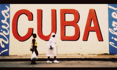 Two Cubans walk by a large sign that says "CUBA" as the U.S. tries to improve relations with Cuba.