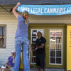 A woman hangs a banner outside her business marking that dispensary as the "First Legal Cannabis Store" in Washington.