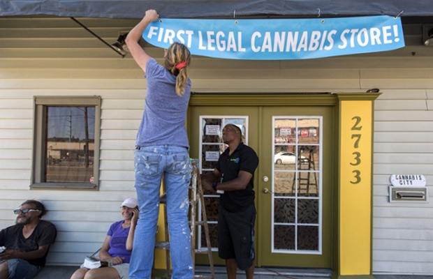 A woman hangs a banner outside her business marking that dispensary as the "First Legal Cannabis Store" in Washington.