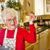 Nonna Marijuana Wears a Red Shirt and Apron While Smiling and Holding Up a Tasting Spoon