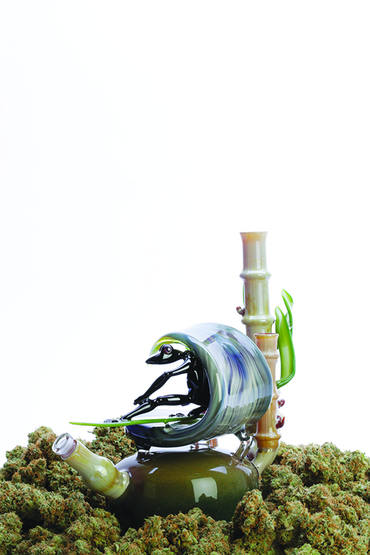 A Glass Piece with Bamboo and a Frog in a Wave by Kimmo Glass Sits on a Bed of Buds