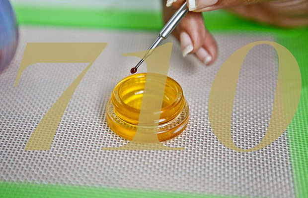 A woman places cannabis concentrate onto a nail from a container on an oil slick. The numer "710" overlays the image.