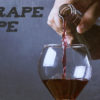 A hand pours a red wine, that has flavors played off of the Grape ape strain, into a wine glass.