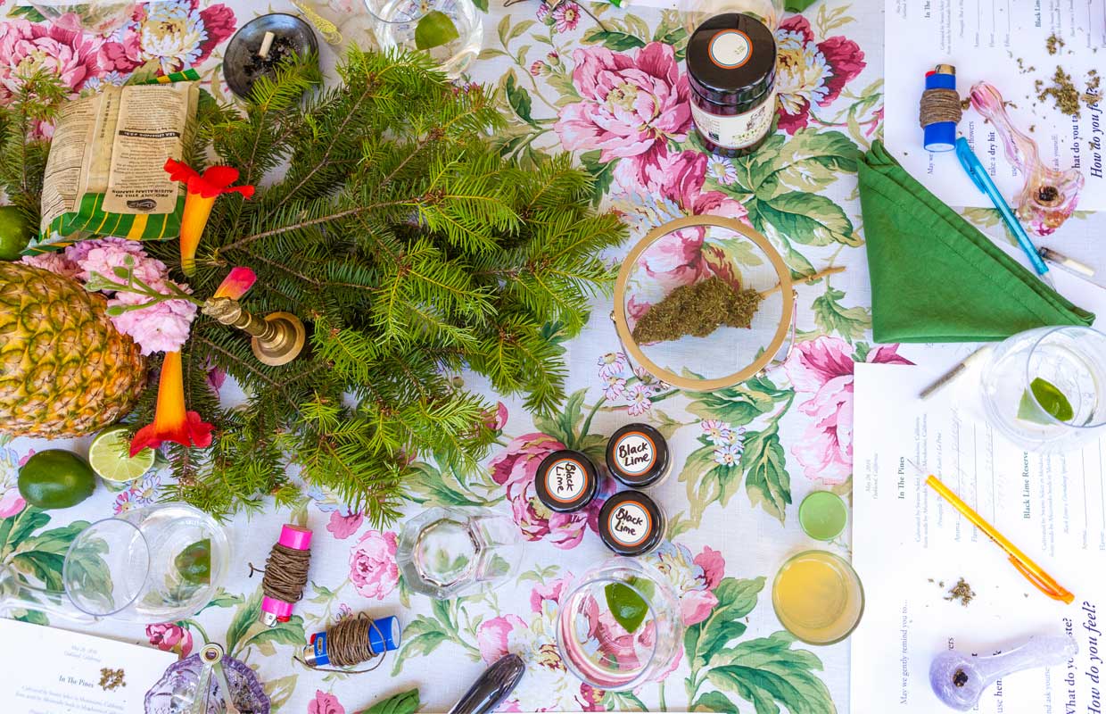 A flower table cloth serves as a backdrop for all of the materials needed at a Flower Girl's tasting session, including a pipe, hempwicks, and bud.