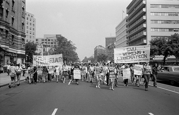 Feminists march in the street carrying signs demanding equality in the 60s.