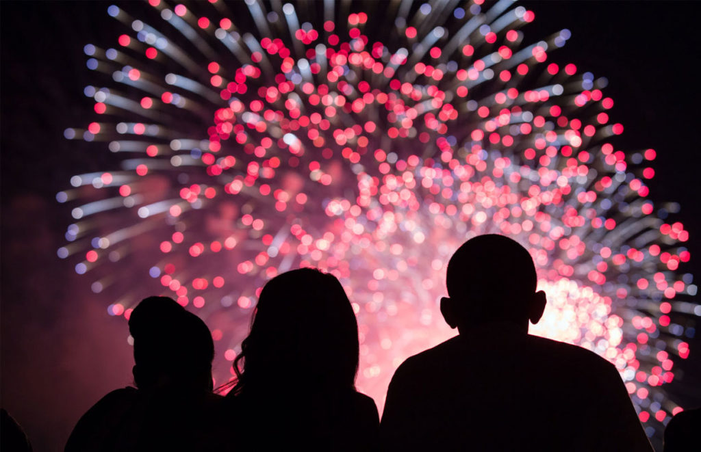 A shilloutted family sits in front of fireworks show on the 4th of July after a picnic filled with cannabis edibles.